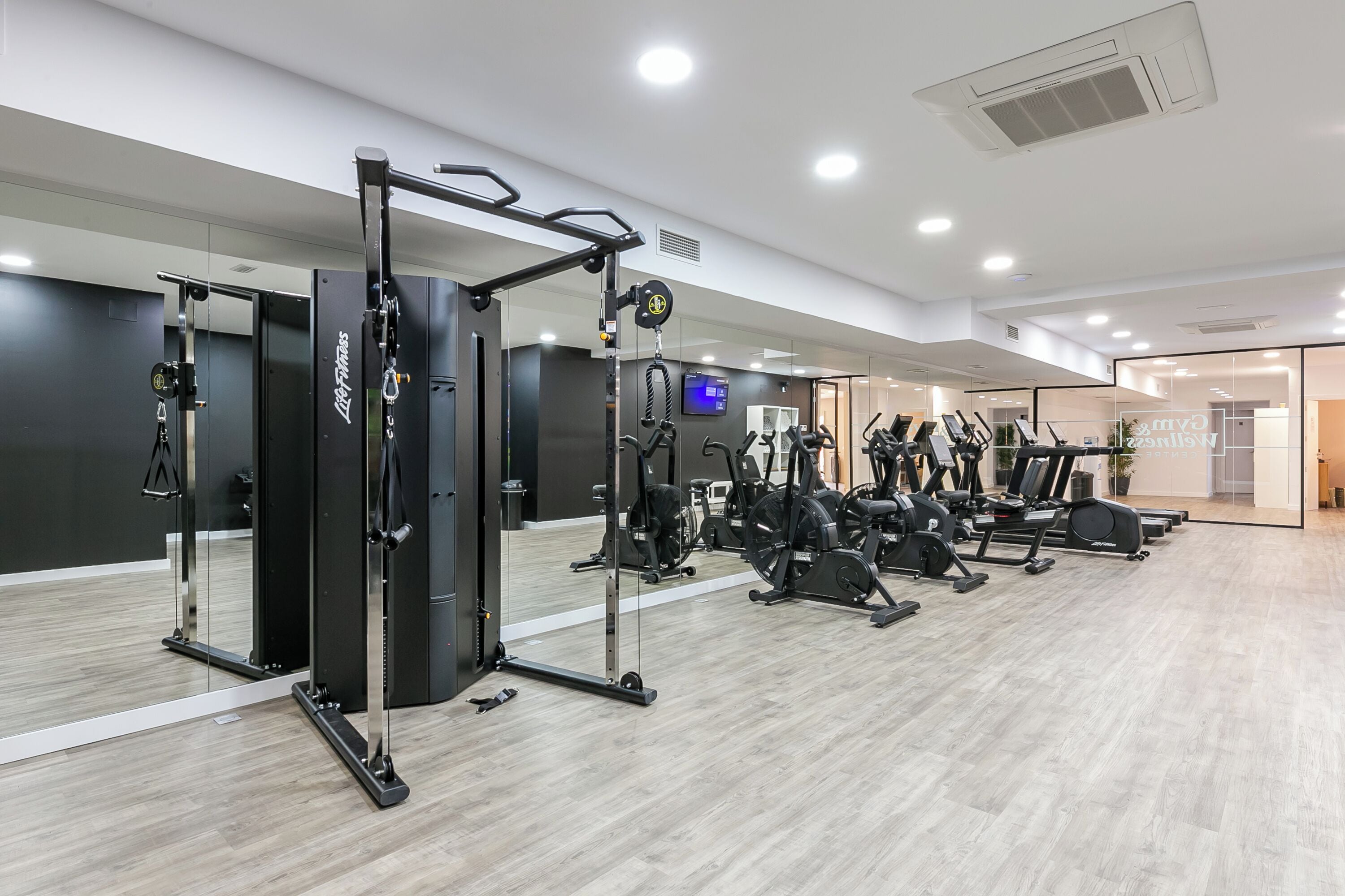 Un gimnasio moderno con diverso equipo de ejercicio, que incluye una jaula de sentadillas, cintas de correr y bicicletas estáticas.