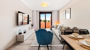 Una sala de estar moderna con televisión, sofá, mesa de comedor y vistas a un balcón.