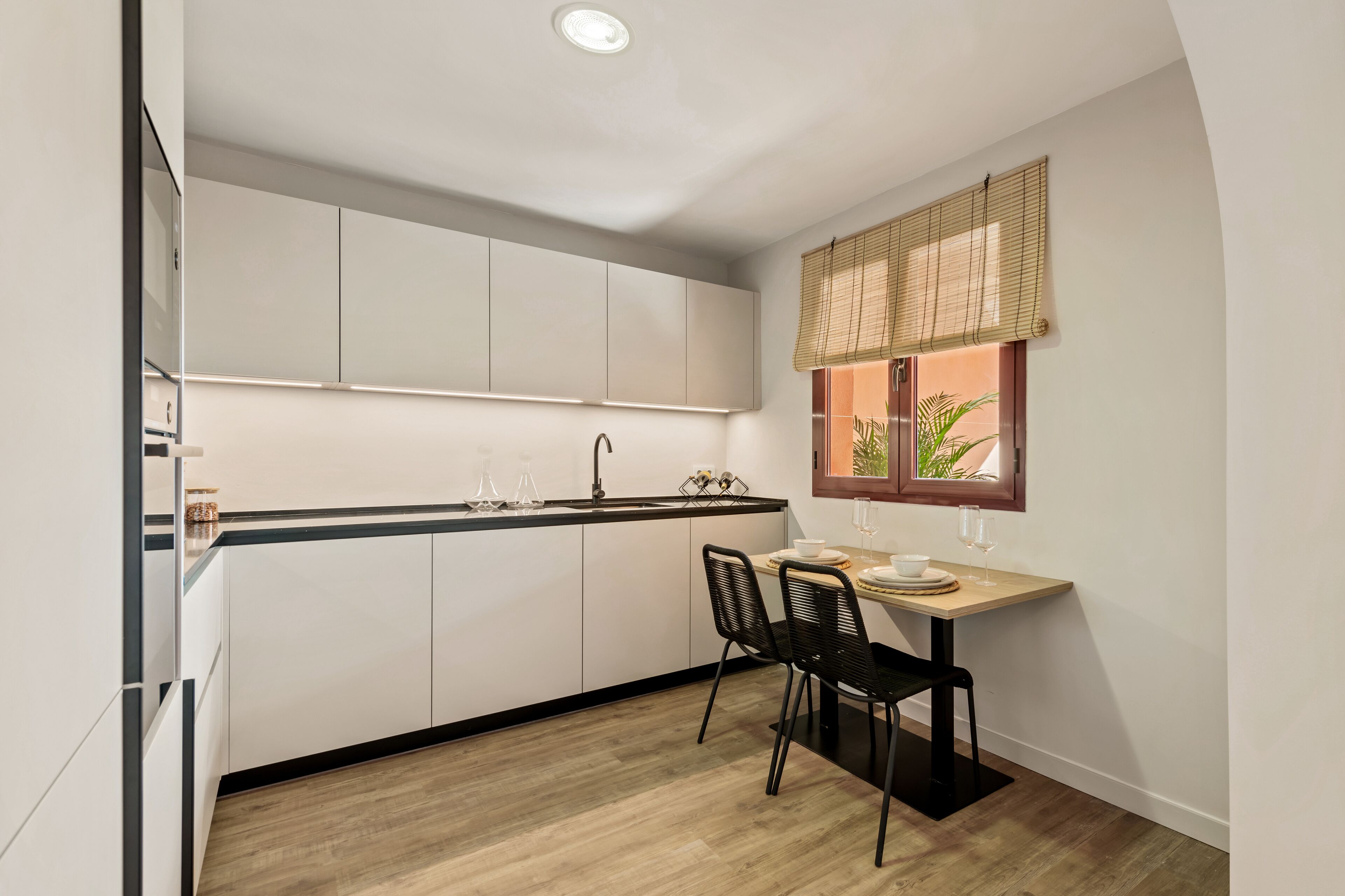 A compact kitchen with white cabinets, a black countertop, and a dining area with two chairs and a small table.