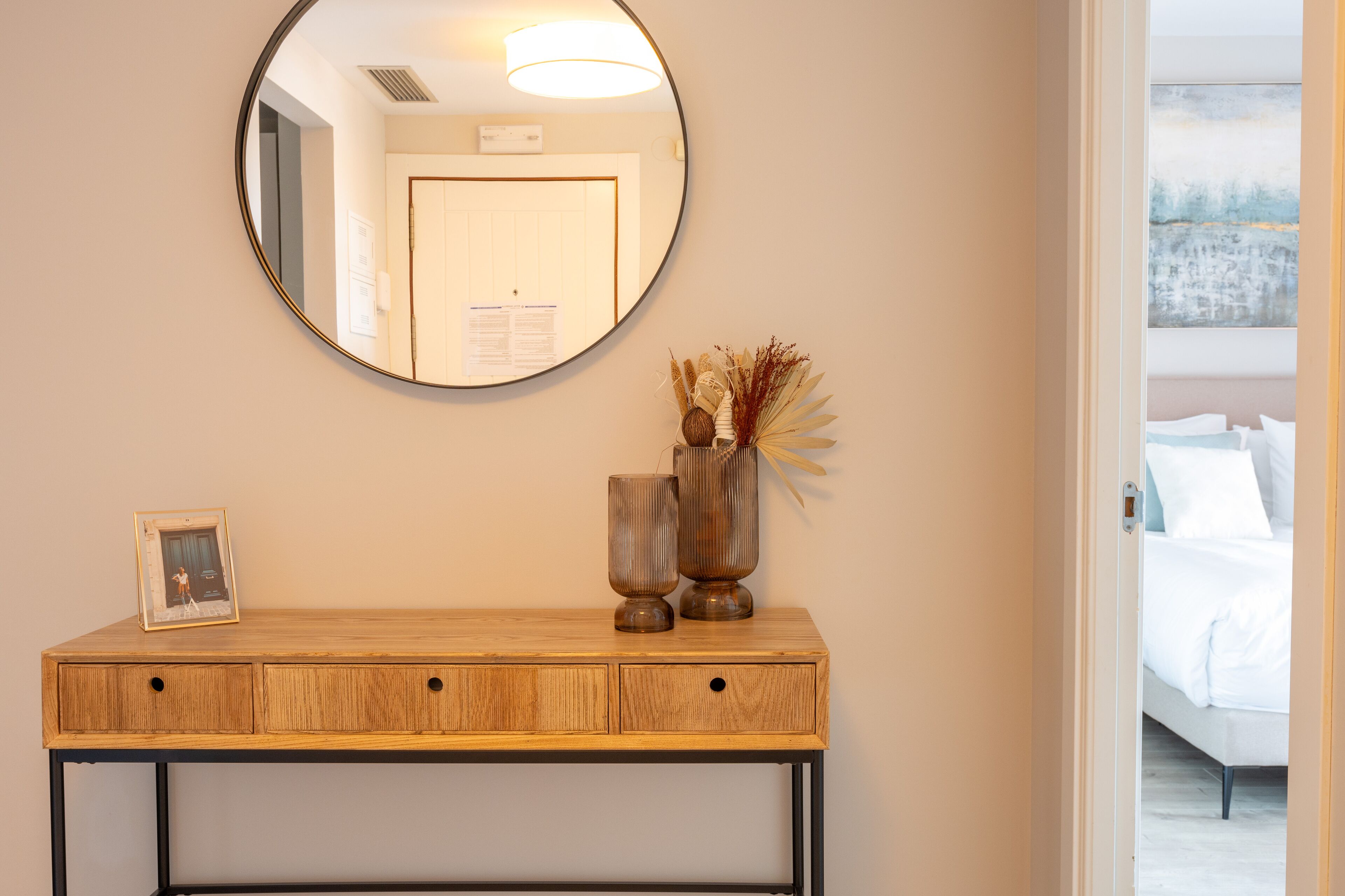 A wooden console table with a mirror above it, a framed picture, and two decorative vases.