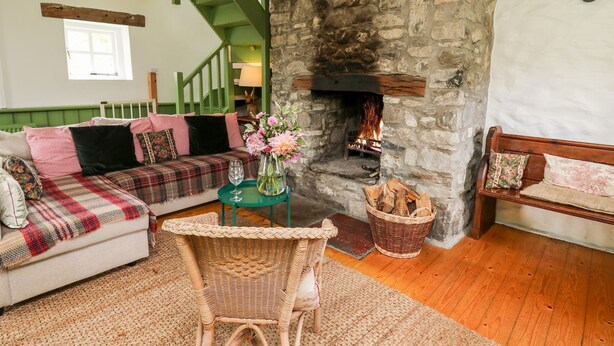 A cozy living room with a stone fireplace, a green staircase, and a wicker chair. - Red Kite Lodge (Llandeilo)