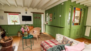 A cozy room with a green door, a wicker chair, a sofa with patterned cushions, and a small table with a vase and glasses. - Red Kite Lodge (Llandeilo)