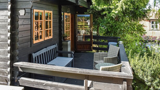 A wooden cabin with a porch, wicker furniture, and a view of the surrounding greenery.
