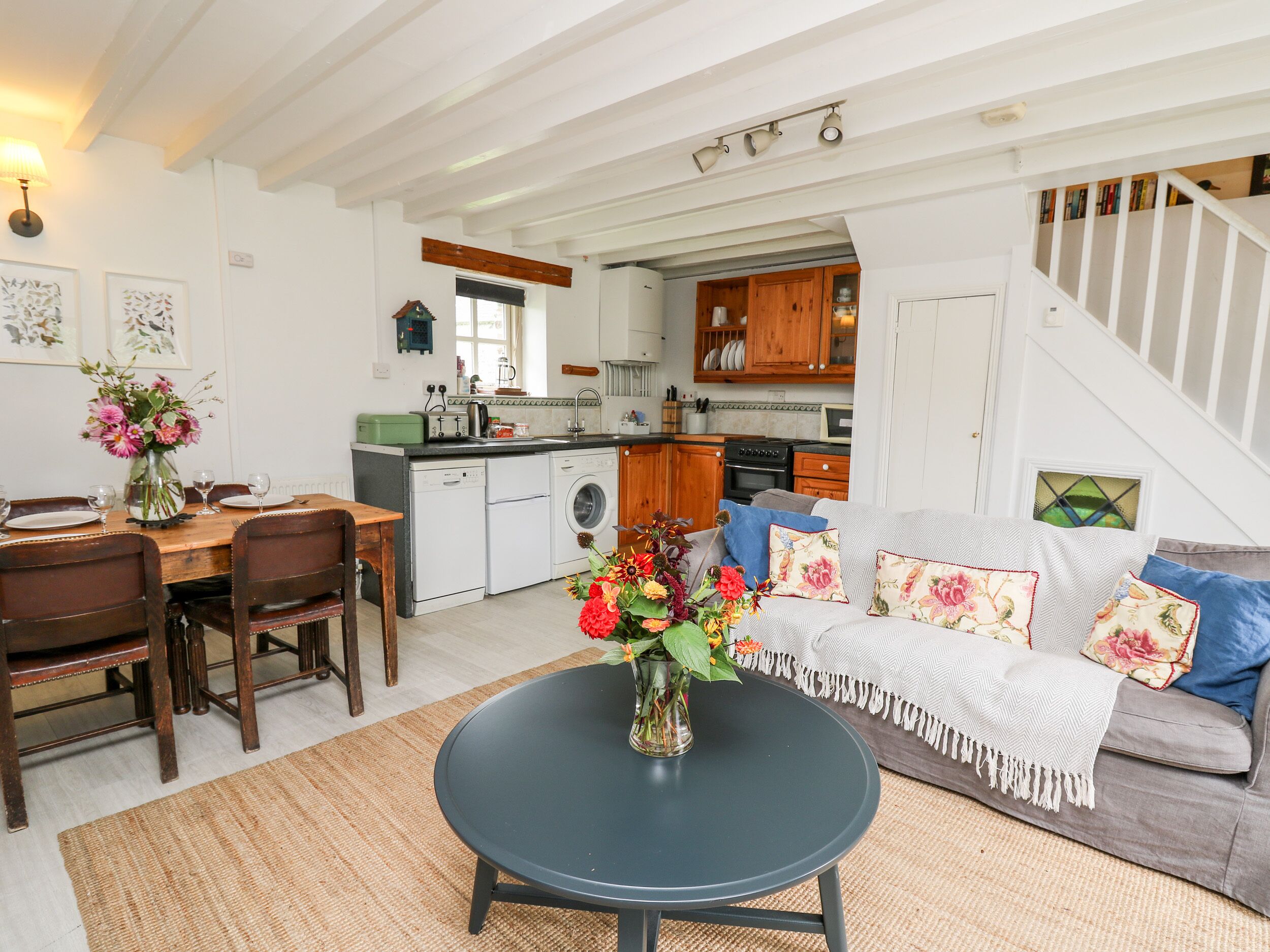 A cozy living room with a dining area, a kitchen in the background, and a staircase leading to an upper floor.