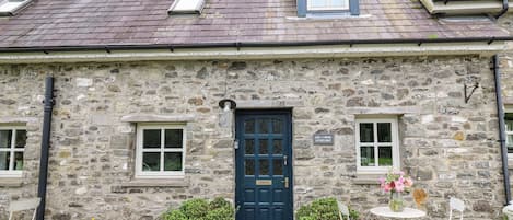 Un edificio de piedra con una puerta azul oscuro, dos ventanas y un tragaluz pequeño.
