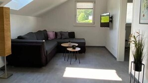 En moderne stue med en modulsofa, et lille rundt bord og et tv ophængt på væggen.