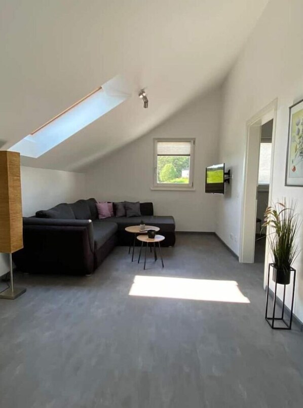 A modern living room with a sectional sofa, a small round table, and a TV mounted on the wall. - holiday flat "Louis" (Passau)