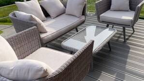 A deck with wicker furniture, including a sofa and chairs, overlooking a green landscape. - roof terrace flat "Alois" (Passau)