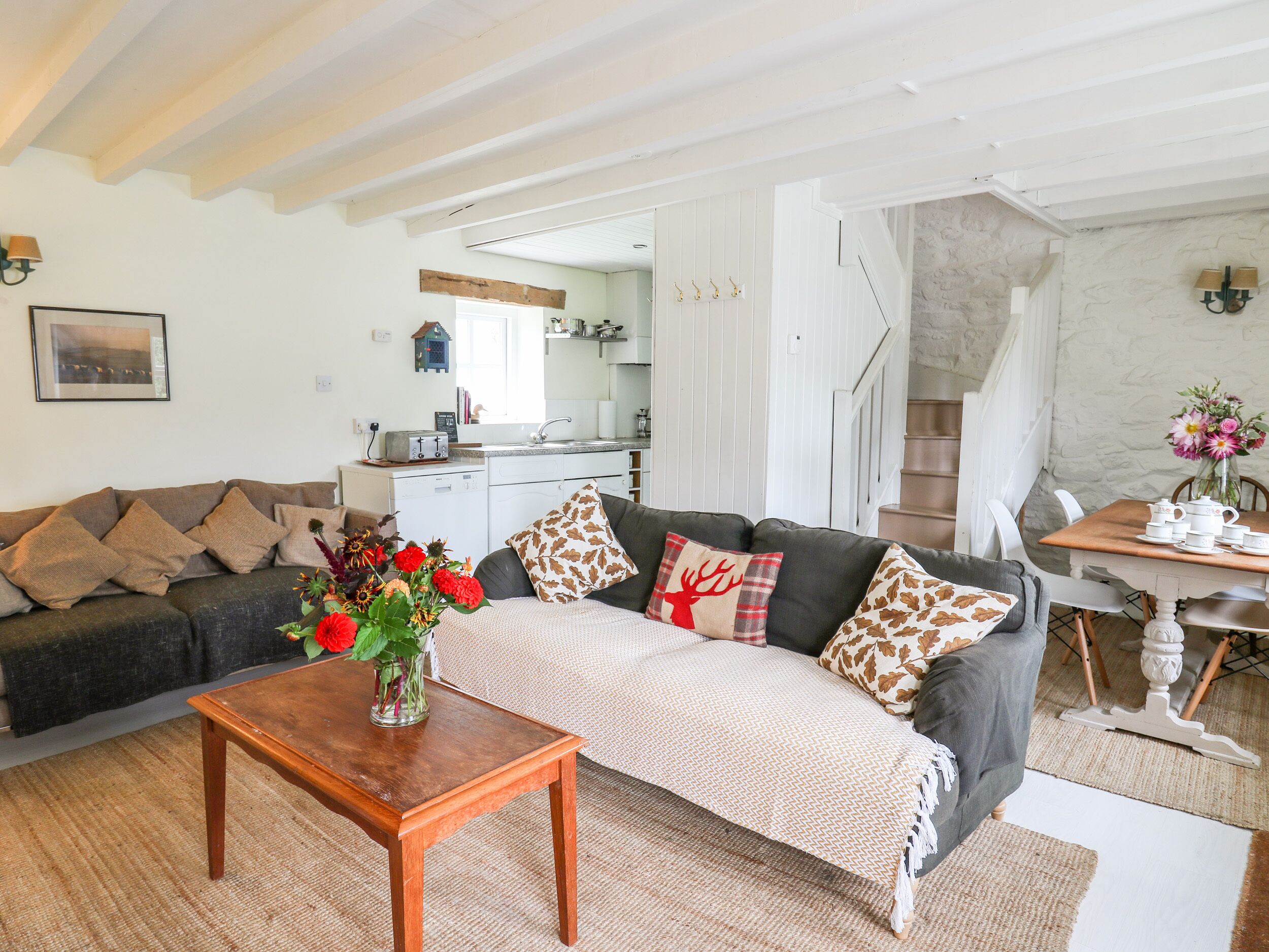 A cozy living room with a sofa, a coffee table, and a dining table with chairs. There is a kitchen in the background with a staircase leading to another level.