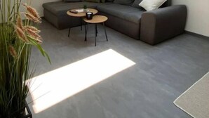 A modern living room with a grey sectional sofa, a small round table, and a potted plant. - holiday flat "Valentin" (Passau)