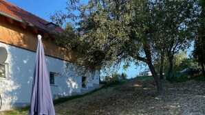 An outdoor patio with a table and chairs, a purple umbrella, and a stone pathway leading to a building with a tiled roof. - holiday flat "Valentin" (Passau)