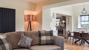 A modern living room with a sofa, a floor lamp, and a dining area with chairs and a table. - 3 bedroom accommodation in Lancaster (Lancaster)