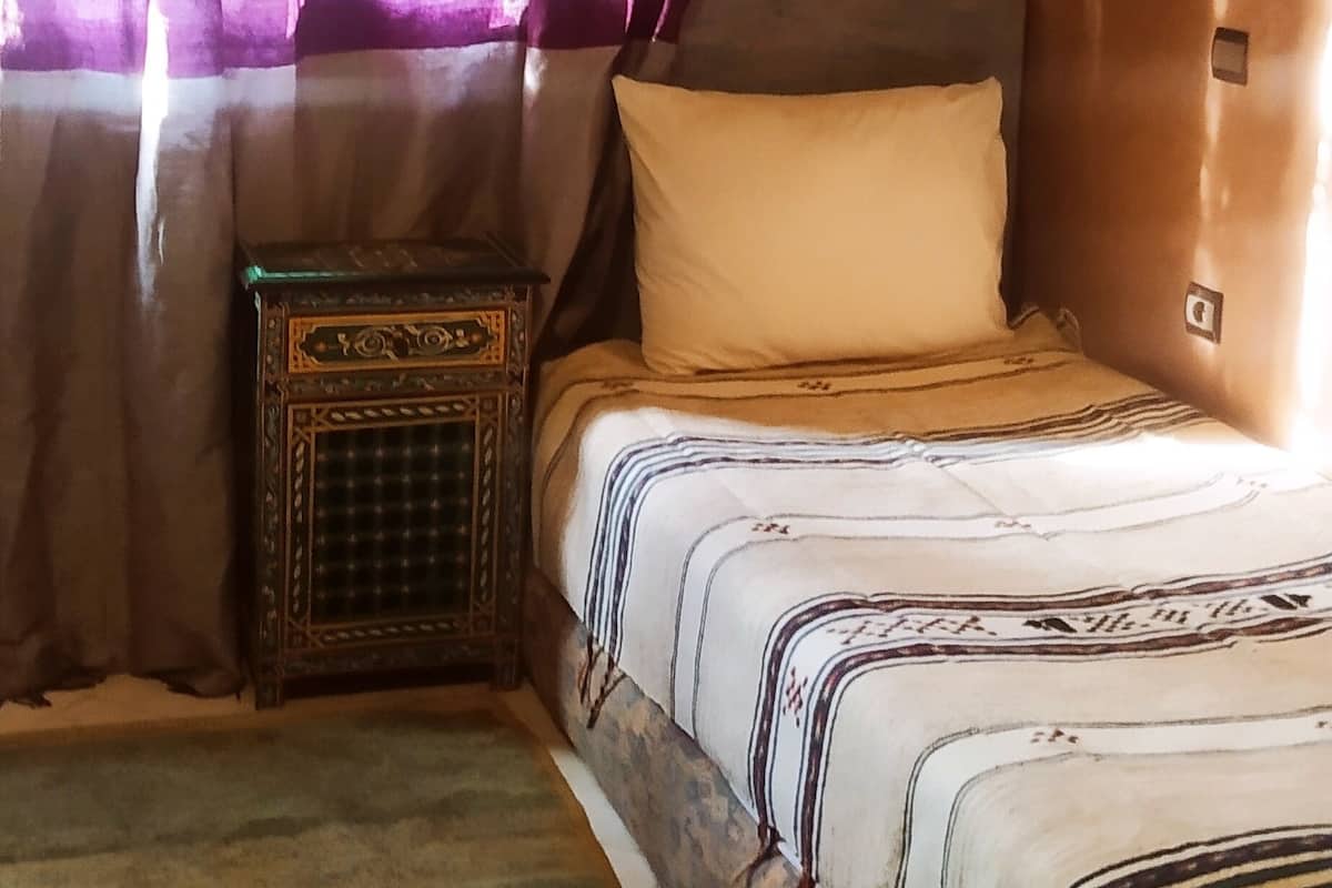 A bedroom with a bed, curtains, a small table, and a patterned rug.
