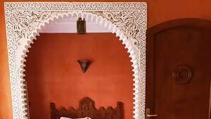 A room with a bed, a door, and a woven stool.