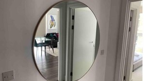 Un miroir rond fixé au mur, qui reflète une pièce comprenant une table à manger, des chaises et un canapé.