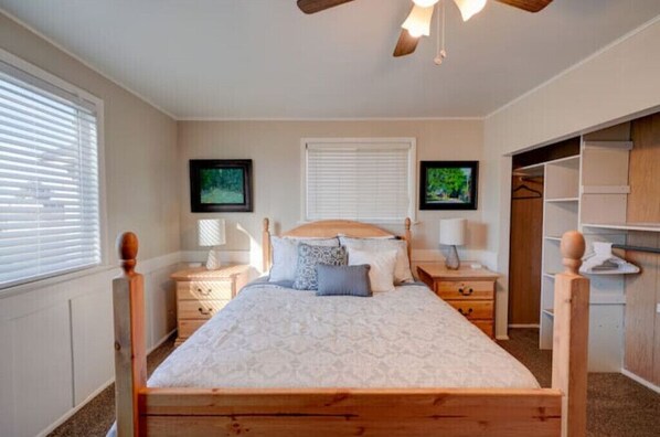 Un dormitorio con una cama de madera, dos mesitas de noche, un ventilador de techo y un vestidor.