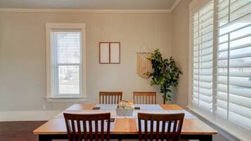 A dining room with a wooden table and chairs, a window with blinds, and a hanging plant.