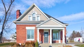 A two-story brick house with a gabled roof, a front porch, and a chimney.