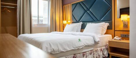 A hotel room with a bed, a wooden nightstand, a mirror, and an air conditioning unit.
