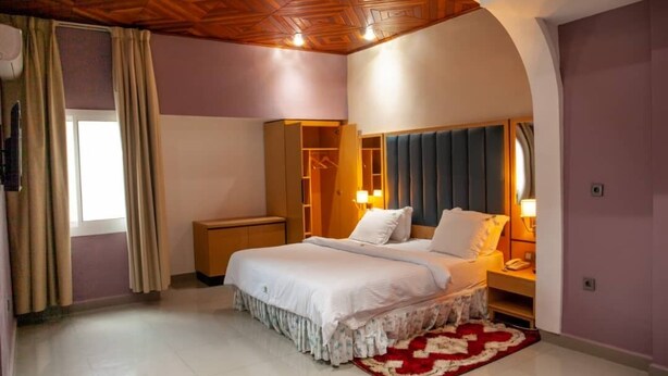 A bedroom with a bed, bedside tables, a wardrobe, and a window with curtains. - Hôtel  Mickel (Douala)