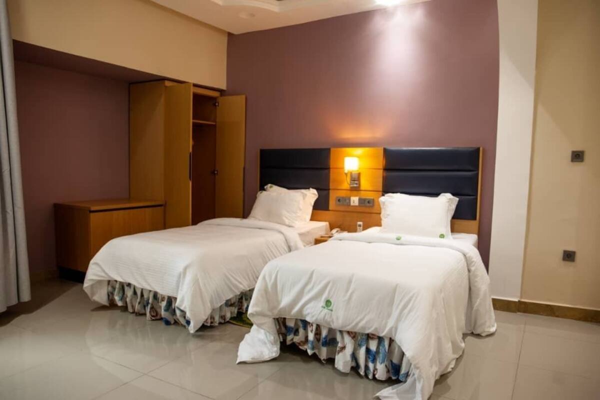 A hotel room with two beds, a wardrobe, and a nightstand with a lamp.