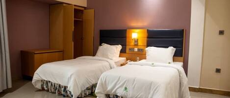 A hotel room with two beds, a wardrobe, and a nightstand with a lamp.