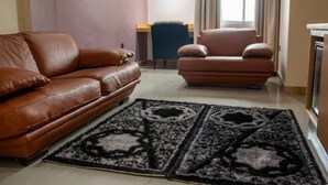 A living room with a brown leather sofa, a matching armchair, and a black and white patterned rug. - Hôtel  Mickel (Douala)
