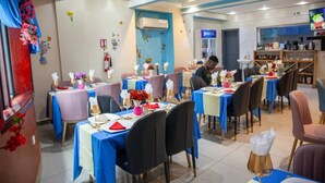 A restaurant with multiple tables, blue tablecloths, and black chairs. - Hôtel  Mickel (Douala)
