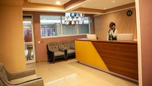 A reception area with a wooden reception desk, a television mounted on the wall, and a seating area with two sofas. - Hôtel  Mickel (Douala)
