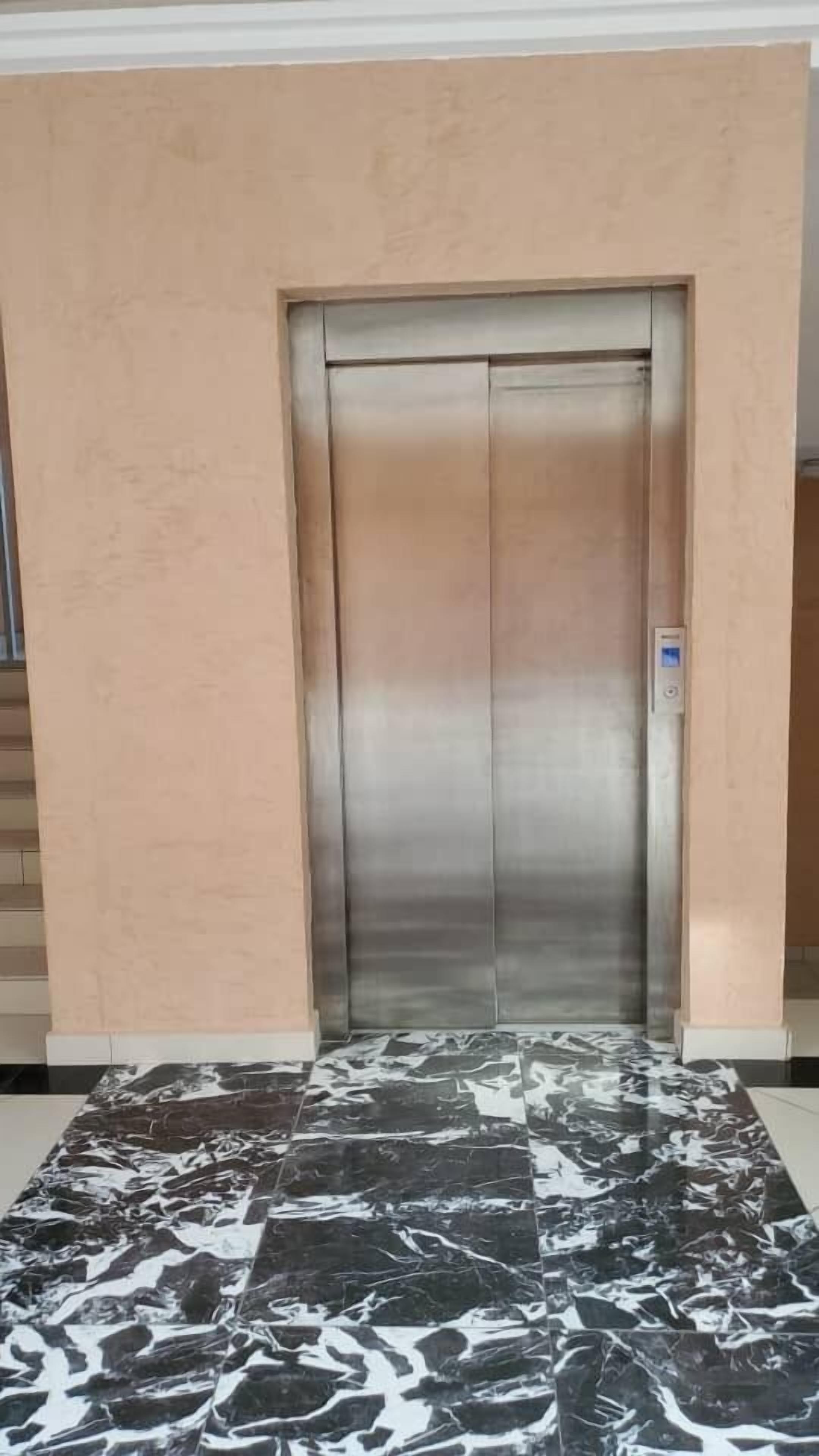 An elevator with a metallic finish, a control panel, and a marble-patterned floor.