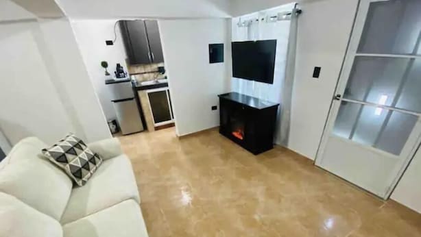 Una sala de estar con sofá, chimenea, televisor y cocina al fondo.