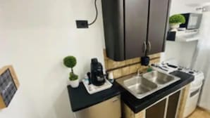 Una cocina compacta con encimera negra, pileta de acero inoxidable y un refrigerador pequeño.