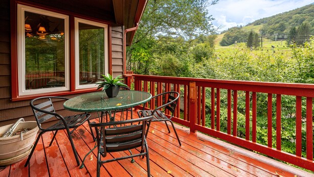 Un terrazzo in legno con ringhiera rossa, un tavolo in vetro e sedie, e vista su un paesaggio verde.