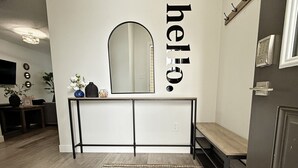 A modern entryway with a bench, a mirror, and a 'hello' sign on the wall. - Beautiful 3 King Beds|Garage|Airport|Disney+ (Edmonton)