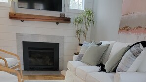 A living room with a white sofa, a wooden floor, a striped rug, a fireplace, and a TV mounted on the wall. - Lake Getaway at Coventry Lake! close to Uconn (Coventry)