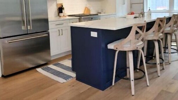 A modern kitchen with white cabinets, a stainless steel refrigerator, a blue island, and wooden bar stools. - Lake Getaway at Coventry Lake! close to Uconn (Coventry)