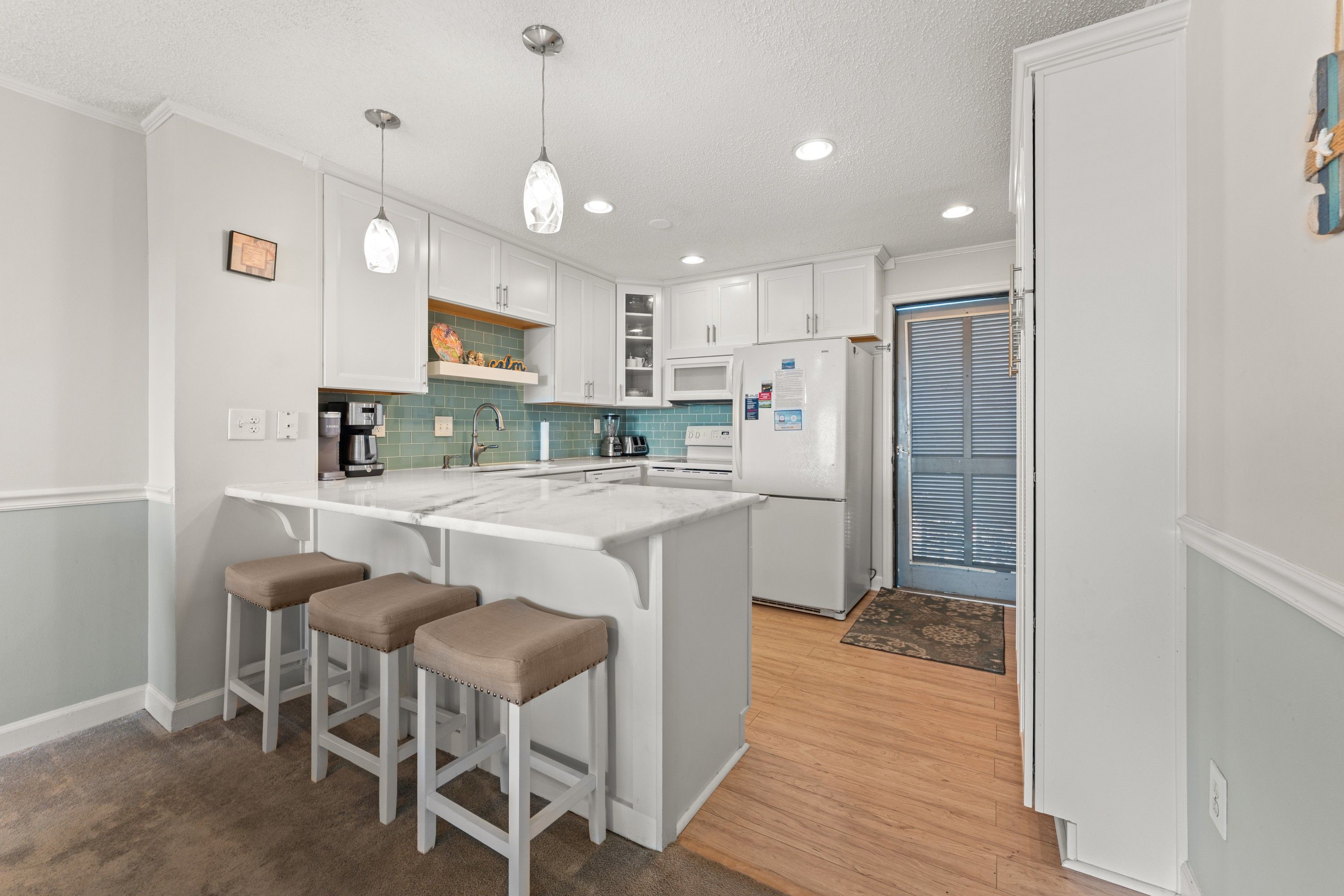 A modern kitchen with white cabinetry, a central island with stools, and a built-in oven.