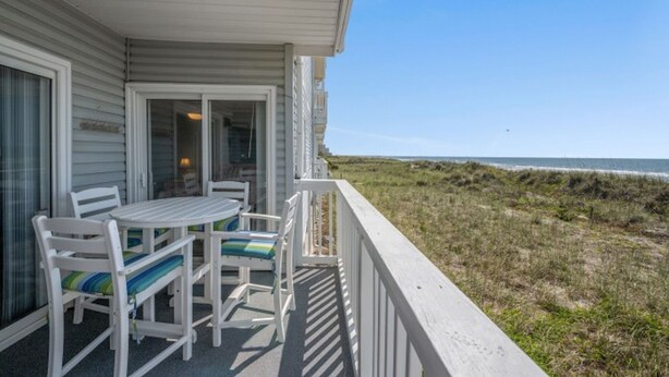 A covered outdoor area with a table and chairs, overlooking a beach. - Beachmaster 104-2BR Oceanfront Condo (North Myrtle Beach)
