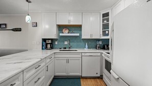A modern kitchen with white cabinets, a blue backsplash, and a wooden floor. - Beachmaster 104-2BR Oceanfront Condo (North Myrtle Beach)