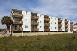 A multi-story residential building with balconies, a palm tree, and a grassy area in front. - Beachmaster 104-2BR Oceanfront Condo (North Myrtle Beach)