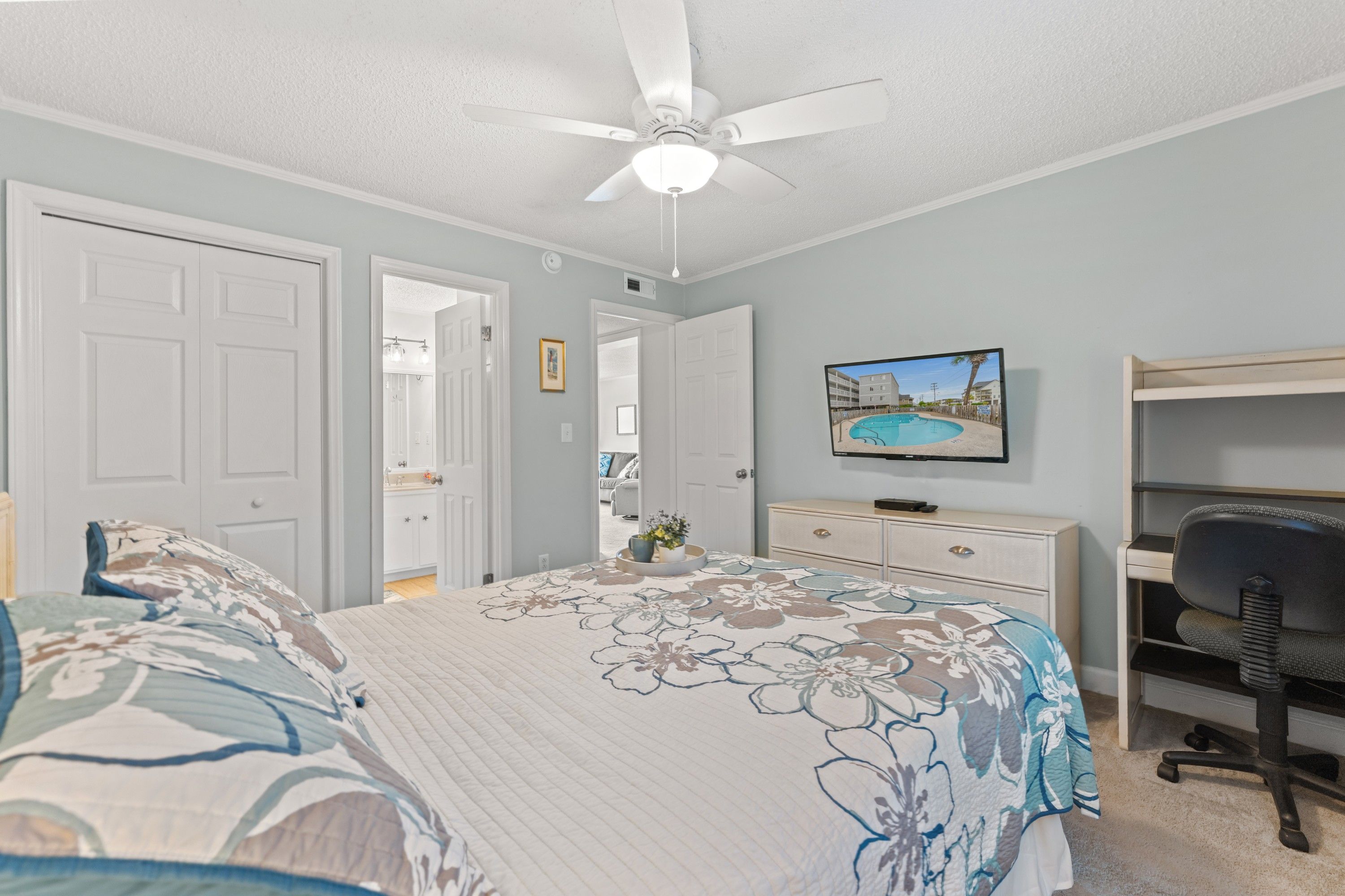 A bedroom with a bed, a desk, a chair, and a ceiling fan.