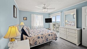 A bedroom with a bed, a ceiling fan, a TV, a dresser, and a balcony with a view. - Beachmaster 104-2BR Oceanfront Condo (North Myrtle Beach)