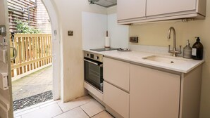 A compact kitchen with white cabinets, a built-in oven, a sink with a modern faucet, and a small countertop. - Hapton Folly (Waterlooville)