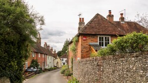 A narrow street lined with traditional brick houses, stone walls, and lush greenery. - Hapton Folly (Waterlooville)