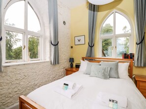 A bedroom with a large bed, two windows, a nightstand, a lamp, and a framed picture on the wall. - Hapton Folly (Waterlooville)