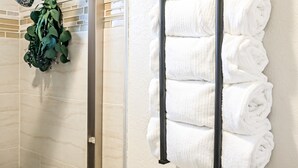 Une salle de bain avec un porte-serviettes où sont rangées des serviettes pliées et un espace douche équipé d’une pomme de douche et agrémenté de plantes vertes.