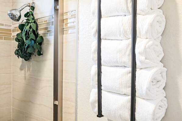A bathroom with a towel rack holding neatly folded towels and a shower area with a showerhead and green plants. - Work and Gym Hideaway (San Jose)