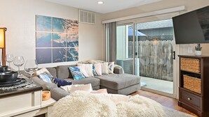 Un salon moderne avec un canapé d’angle gris, un tapis blanc moelleux et un téléviseur à écran plat posé sur un meuble en bois.