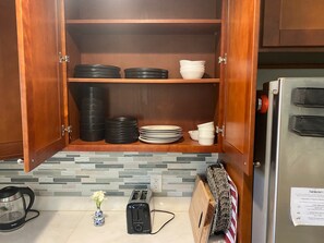 A kitchen with a wooden cabinet containing black and white plates, bowls, and a toaster.