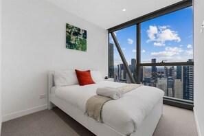 Enjoy a panoramic city view from the comfort of this stylish room with a large window, a neatly made bed, and a cozy throw blanket.